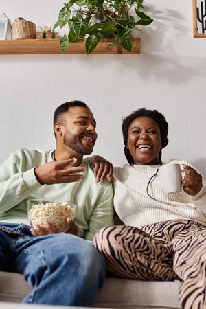 A happy couple shares laughter and warmth in their cozy living room, savoring snacks together.の写真素材
