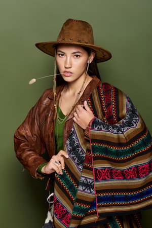 Young woman confidently poses in a fashionable outfit with a vibrant shawl and hatの写真素材