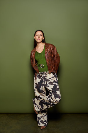 Beautiful young woman poses stylishly in cow print pants and a green top, radiating charm.の写真素材