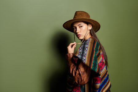 A charming young woman in a colorful poncho and hat stands out against a bold green backdrop.の写真素材