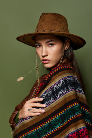 A young woman flaunts her style in a striking hat and vibrant poncho in a tranquil scene.の写真素材