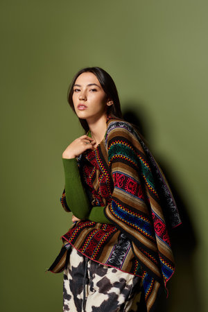 Confident young woman showcases her style with a beautiful shawl while posing gracefully indoorsの写真素材