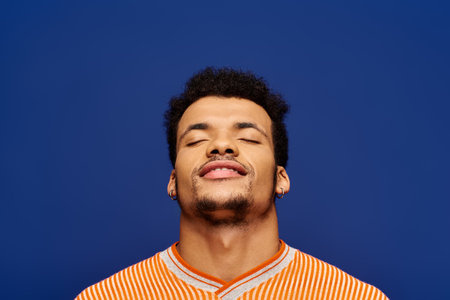 A charming young man with eyes closed, relishing a peaceful moment in front of a blue backdrop.の写真素材