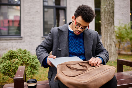 Stylish individual checks his laptop while seated on a wooden bench in a vibrant park.