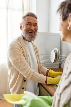 Mature couple smiles and enjoys quality time together while washing dishes side by side.の写真素材