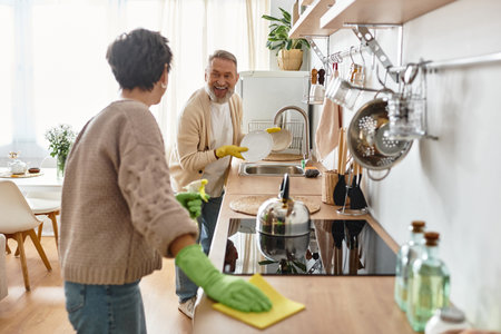 Couple happily cleans their kitchen, sharing smiles and teamwork in their bright home.の写真素材