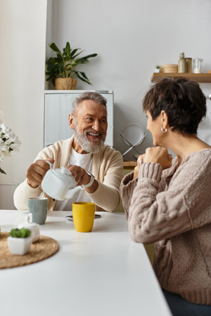 A mature couple shares laughter and conversation while sipping coffee at their kitchen table.の写真素材