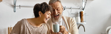 Happy couple sharing a light moment while sipping coffee in their modern kitchen.の写真素材