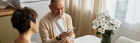 Mature couple shares smiles and laughter while looking at a device in their cozy home.の写真素材