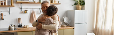 A senior couple enjoys a tender hug in their beautifully decorated kitchen, filled with warmth.の写真素材