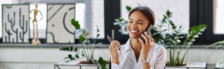 A young Black woman in a white shirt chats animatedly on the phone while working, banner