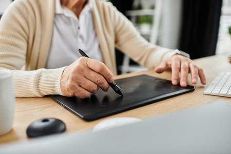 Handsome senior man creates digital art using a tablet in a bright, stylish office environment.の写真素材