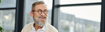 Mature man with glasses and beard smiles warmly, enjoying a moment in a well lit space.の写真素材