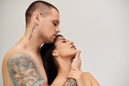 A seductive young woman leans into her shirtless partner, sharing an intimate moment.の写真素材