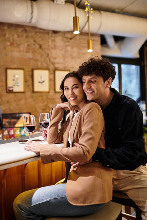 A beautiful young couple celebrates their love at a restaurant, sharing smiles and wine.の写真素材