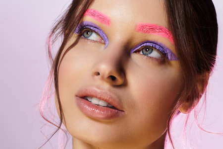 Pretty young woman highlights her unique makeup style with vibrant colors against a grey background.