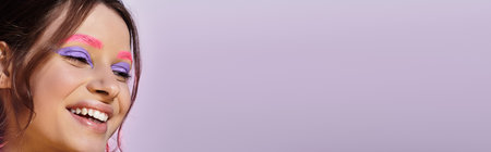Young woman showcases stunning purple eyeshadow and pink eyebrows against a soft grey backdrop, bannerの写真素材