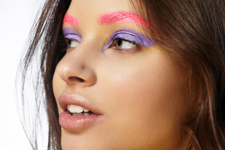 A young woman displays striking beauty with bold purple eyeshadow and pink eyebrows in a studio.の写真素材