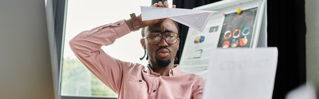 Young African American man struggles with focus while working remotely in a stylish workspace.の写真素材