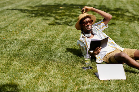 A handsome young man relaxes on the grass, working on his laptop with a drink in hand.の写真素材