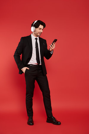 A handsome young man in a suit smiles at his phone, standing against a bold red backdrop.の写真素材