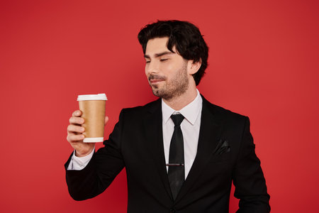 With a confident smile, the young man in a suit admires his coffee cup, radiating charm and style.の写真素材