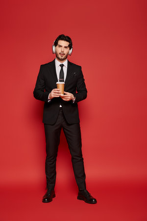 A young, handsome man dressed in a suit holds a coffee cup while wearing headphones.の写真素材