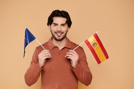 A cheerful young man with brunette hair proudly holds the European and Spanish flags.の写真素材