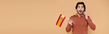 A young man with dark hair shows excitement while holding a Spanish flag and talking on the phone.の写真素材