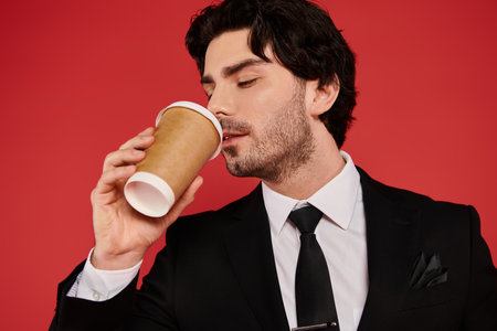 Brunette man enjoys a warm cup of coffee while dressed sharply in a black suit, exuding confidence.の写真素材