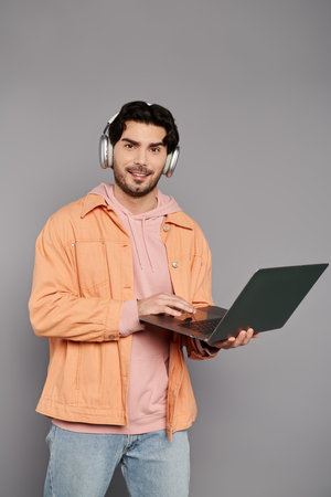 A young man with dark hair and stylish attire engages with his laptop while listening to music.の写真素材