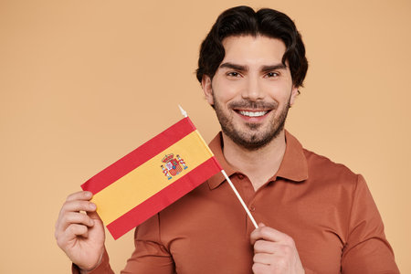 A young handsome man beams with pride as he holds a Spanish flag against a warm backdrop.の写真素材