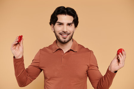 A cheerful young man holds red objects in both hands, radiating joy and playfulness.の写真素材