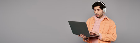 A stylish young man in trendy clothes intently uses his laptop with headphones on.の写真素材