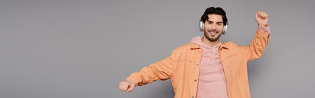 Enthusiastic young man enjoys music while dancing in a stylish gray studio environment.の写真素材
