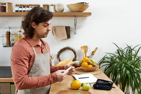 Young man carefully checks his blood sugar while preparing healthy meals at home.