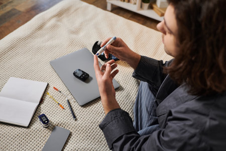 A young man with long hair monitors his blood sugar in a cozy home environment.の写真素材