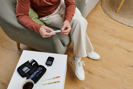 In a stylish apartment, a young man checks his blood sugar while sitting in a cozy chair.