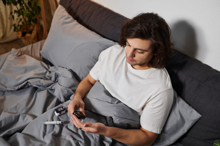 Caucasian man monitors blood sugar levels while relaxing in bed at home.の写真素材