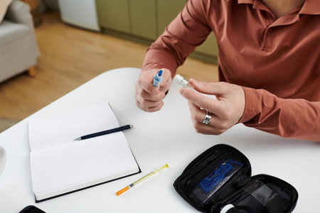 A young man with diabetes prepares insulin while documenting his daily routine at home.の写真素材