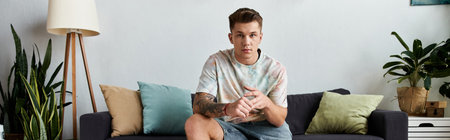 A young handsome man sits comfortably on a couch in a modern living space decorated with plants.の写真素材