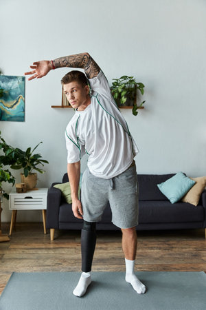 A young man with a prosthetic leg stretches in a bright living room with greenery around him.