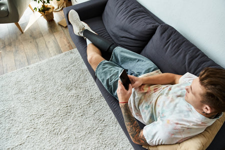 A young handsome man relaxes on a couch while using his phone, showcasing his vibrant personality.の写真素材