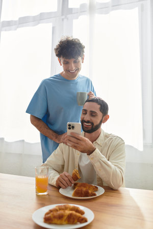 Two men enjoy breakfast in their stylish apartment, sharing smiles and a warm drink while relaxing.の写真素材