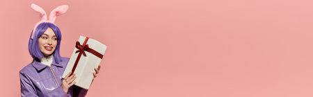 Stylish woman with bunny ears smiles while holding a wrapped gift, creating a cheerful atmosphere.の写真素材