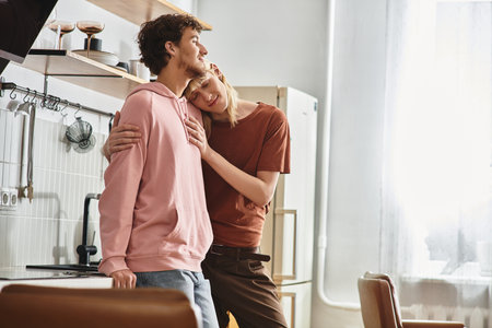 Two loving men embrace in a sunlit kitchen, showcasing their bond and affection for each other.の写真素材