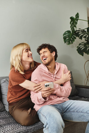A joyful couple enjoys each others company while cuddling on their couch, sharing laughter.の写真素材