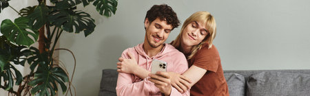 Two men share a joyful moment while embracing each other and looking at their phone.