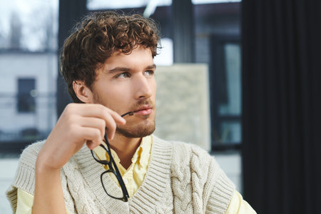 Engaged in work, a young man ponders over tasks while dressed in a stylish sweater vest.の写真素材
