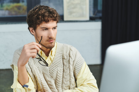 Young professional with curly hair is deep in thought while working at a sleek office desk.